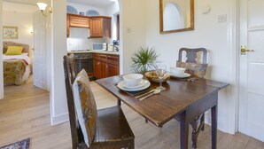 A dining area with a wooden table, chairs, and a mirror above. There is a kitchen visible through an archway in the background. - Little Barton (Taunton)