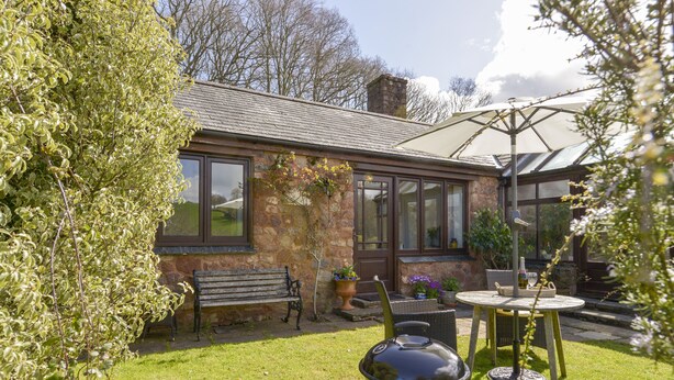 A patio with a grill, a bench, and a table with chairs. - Little Barton (Taunton)