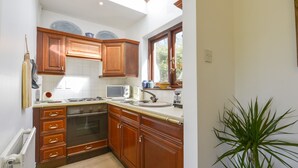 A kitchen with wooden cabinets, a stove, a microwave, and a window. - Little Barton (Taunton)