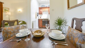 A dining area with a wooden table set for two, a green sofa, and a kitchen in the background. - Little Barton (Taunton)
