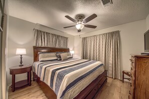 Un dormitorio con cama, ventilador de techo, mesita de noche, cómoda y cortinas.