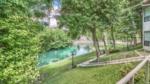 A landscaped area with a pond, trees, and a building with a balcony. - Timeless Tranquility Crc 317 2 Bedroom Condo by RedAwning (New Braunfels)