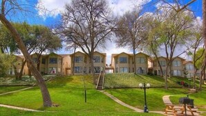 A row of modern, two-story apartment buildings with a grassy courtyard, a picnic table, and a staircase leading to the upper floors. - Timeless Tranquility Crc 317 2 Bedroom Condo by RedAwning (New Braunfels)