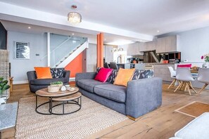 Ein modernes Wohnzimmer mit einem grauen Sofa, einem Couchtisch und einer Treppe, die in eine Küche führt.