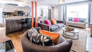 Una sala moderna con sofá, mesa de centro y comedor, con una cocina al fondo.