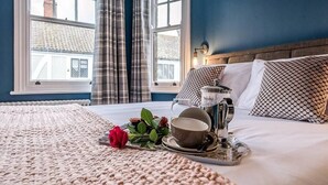 Una cama bien tendida con una bandeja de desayuno, una rosa roja y una taza.
