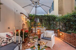 Eine Terrassensitzgruppe im Freien mit Tisch für Zwei, umgeben von Korbmöbeln, Kerzen und einer Obstauslage.