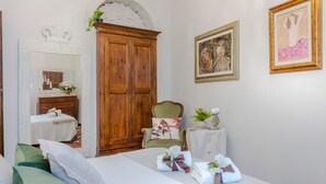 Une chambre d’hôtel avec une grande armoire en bois, un lit avec des serviettes soigneusement pliées, une chaise et deux œuvres d’art encadrées accrochées au mur.