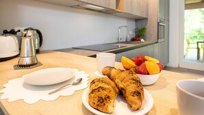 Ett modernt kök med träskåp, en kaffebryggare, en fruktskål med jordgubbar och apelsiner samt croissanter på en tallrik.