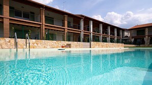 En swimmingpool med en stenmur och en byggnad med balkonger i bakgrunden.