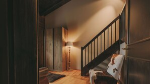 Una escalera de madera con barandilla, una lámpara y un sillón estampado.