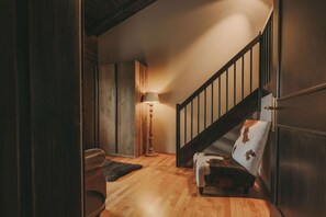 Una escalera de madera con barandilla, una lámpara y un sillón estampado.