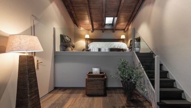 A staircase leading to a loft bedroom with a bed, a lamp, a wicker basket, and a potted plant.