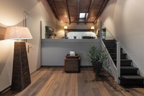 A staircase leading to a loft bedroom with a bed, a lamp, a wicker basket, and a potted plant.