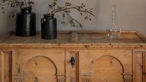 A wooden dresser with three black vases and a clear decanter.