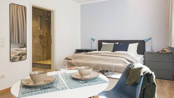 A modern hotel room with a bed, bedside table, and a dining area with a table and chairs.
