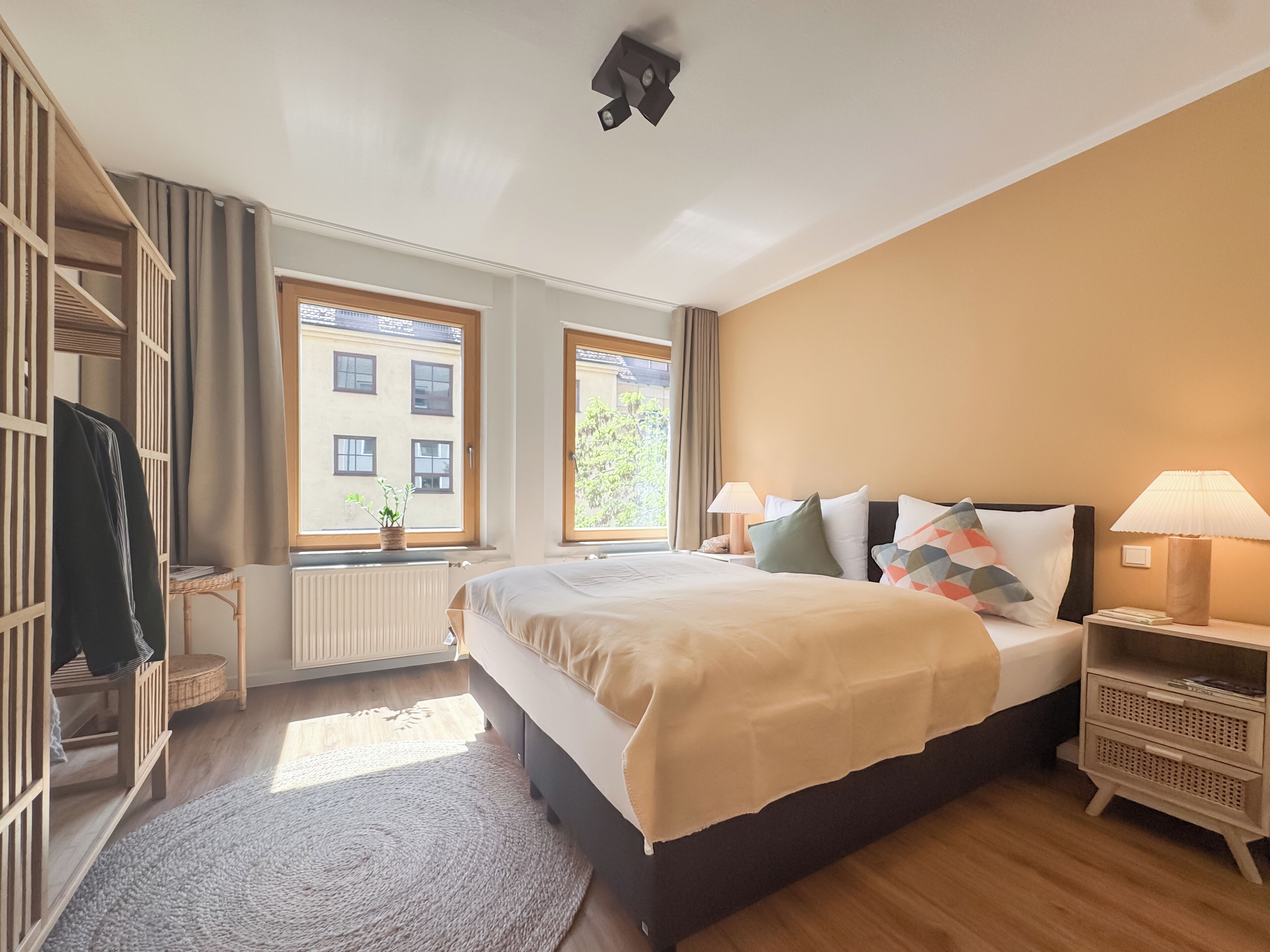 Ein Schlafzimmer mit Bett, Nachttischen, einem Schrank, einem Fenster, einer Heizung und einer Zimmerpflanze.