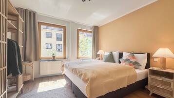 Ein Schlafzimmer mit Bett, Nachttischen, einem Schrank, einem Fenster, einer Heizung und einer Zimmerpflanze.