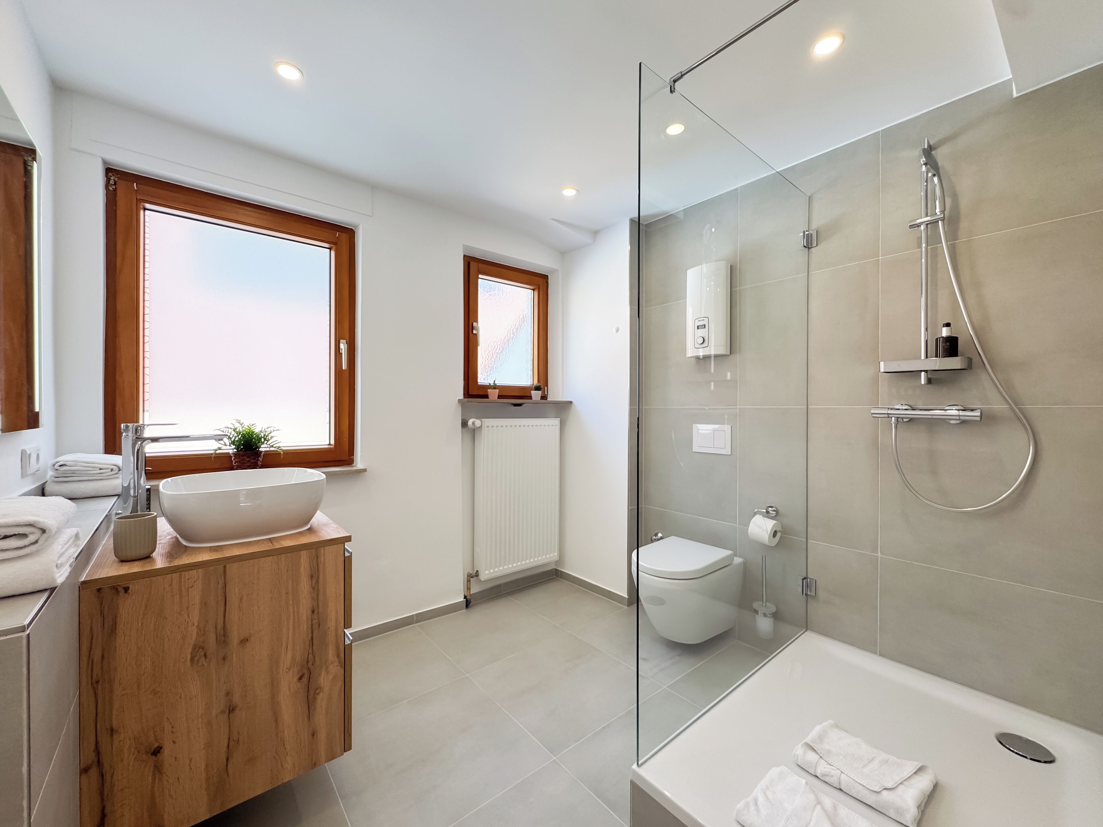 Un baño moderno con ducha envuelta en vidrio, una bañera independiente y un tocador de madera con un lavamanos grande.