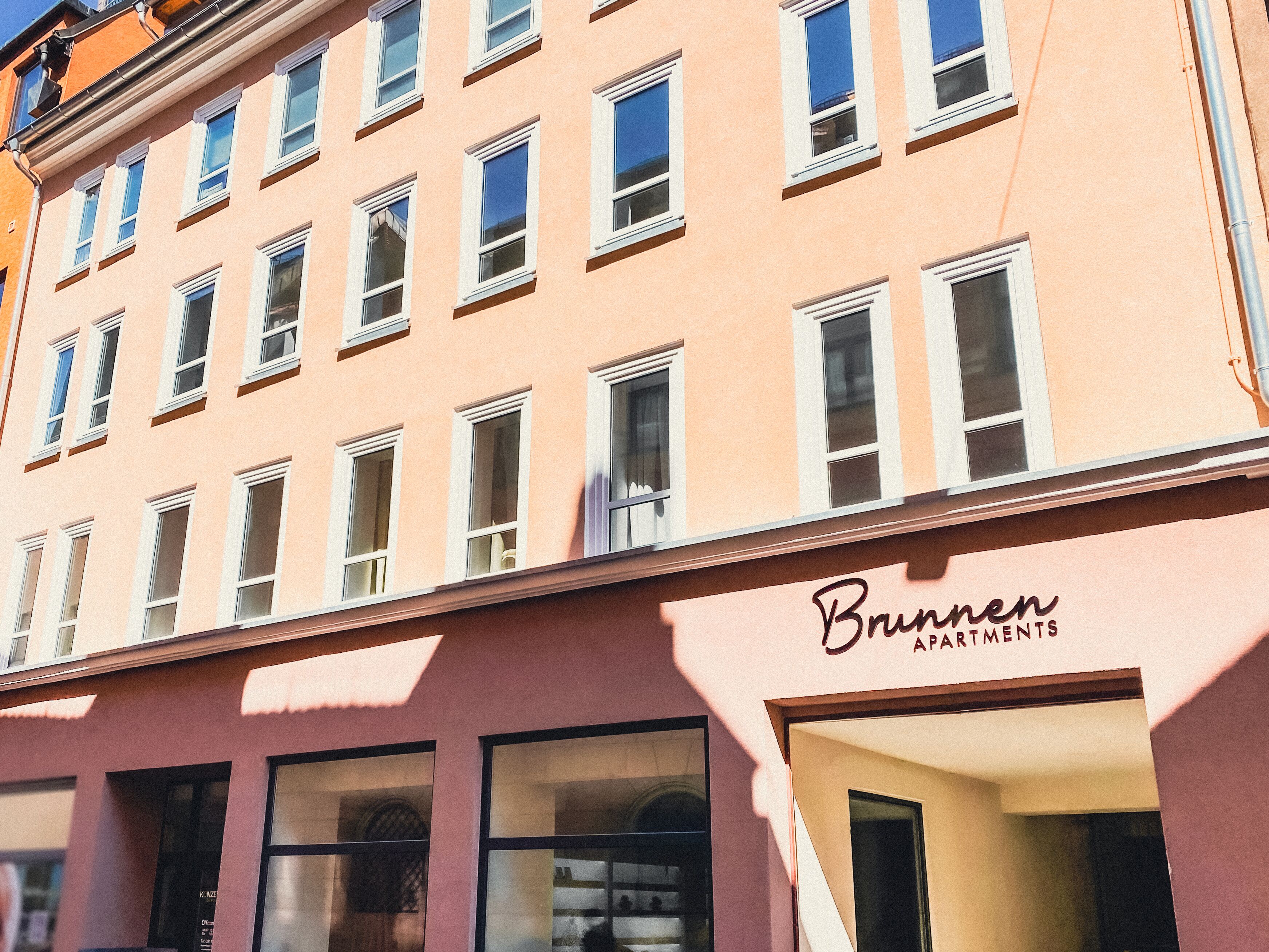 A building with multiple windows and a sign that reads "Brunnen Apartments."