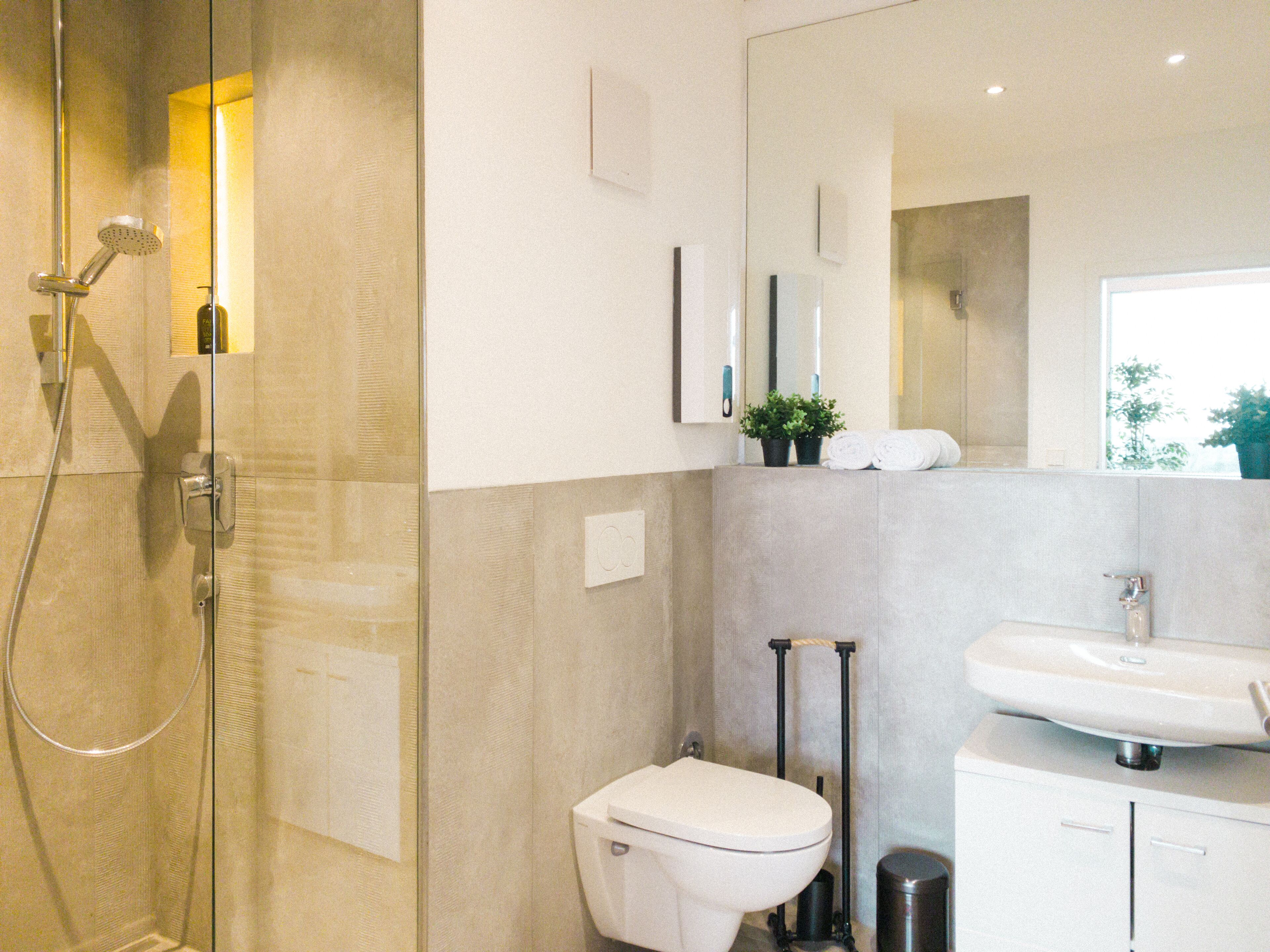 Ein modernes Badezimmer mit Duschkabine, Toilette, Waschbecken und Spiegel.