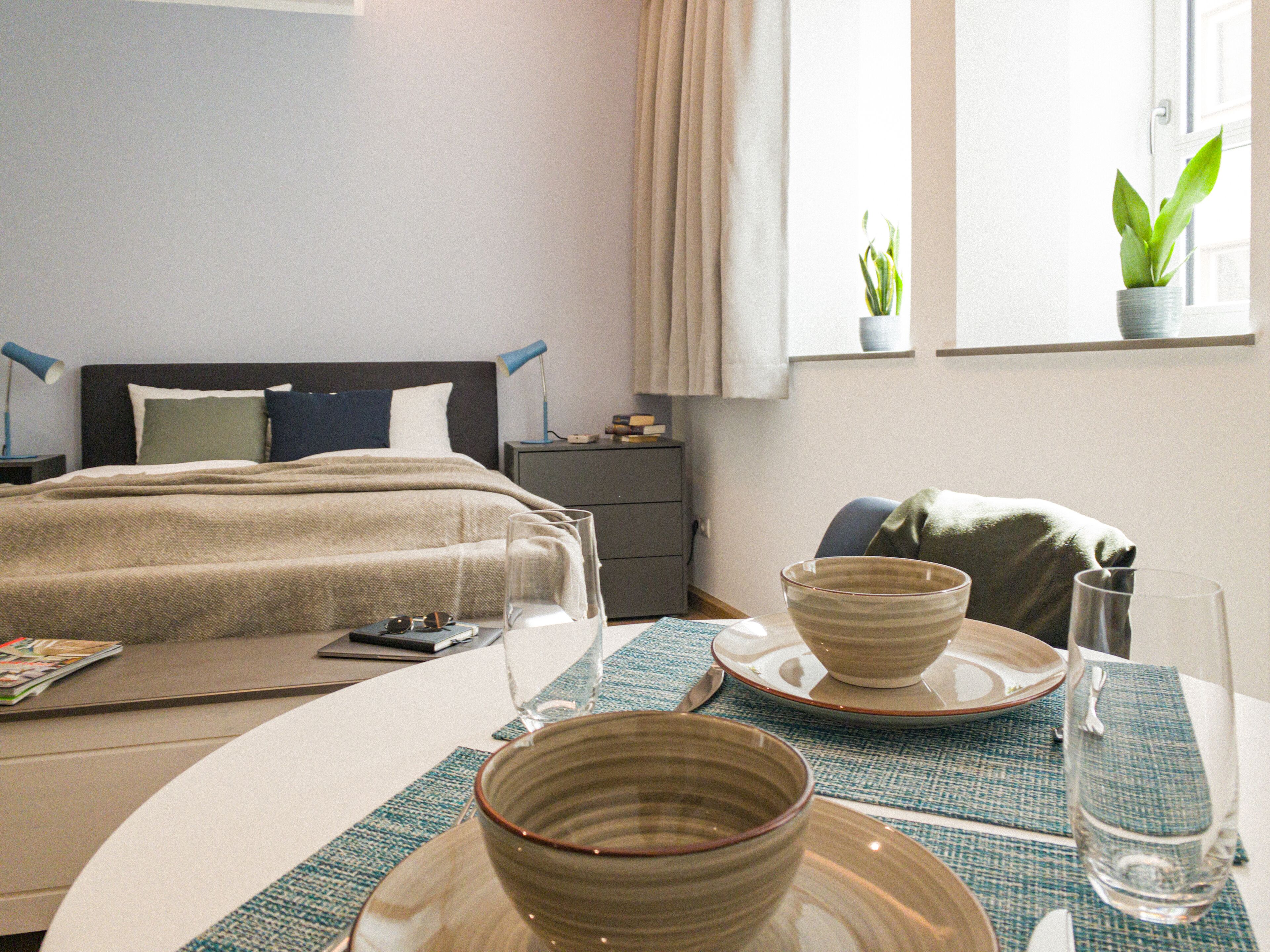 Une chambre d’hôtel comprenant un lit, une table de chevet, une lampe et un coin repas avec une table dressée pour deux personnes.