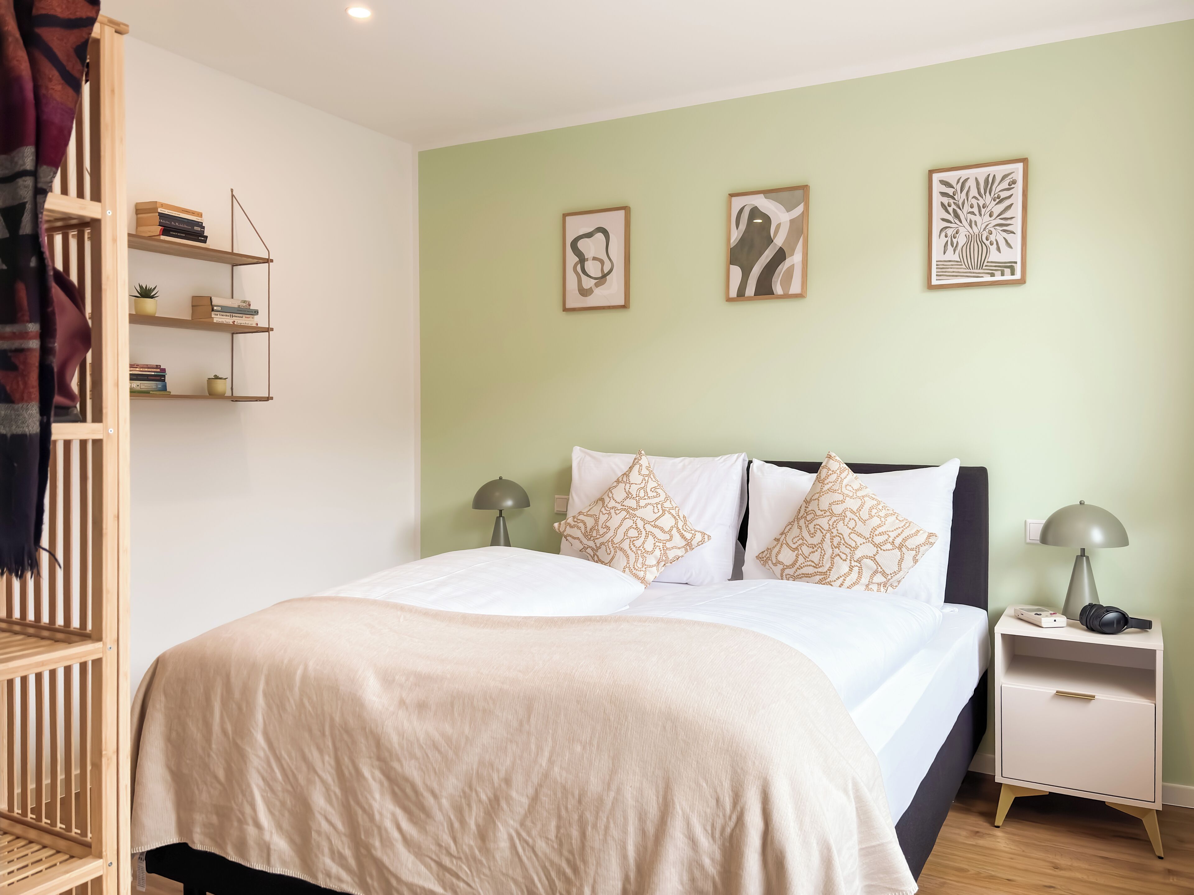 A neatly arranged bedroom with a bed, bedside tables, a nightstand, and a shelf unit.