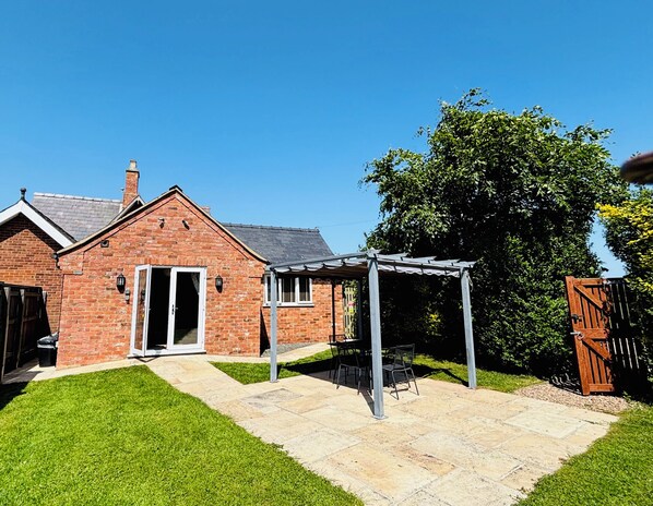 Une maison en briques avec un patio, une pergola et un grand arbre dans le jardin.