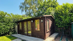 Uma cabana de madeira com vedação de vidro, rodeada por um gramado bem cuidado e uma cerca de madeira.