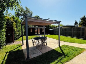 Un patio couvert, équipé d’une table et de chaises, entouré d’une pelouse bien entretenue et d’une clôture en bois.