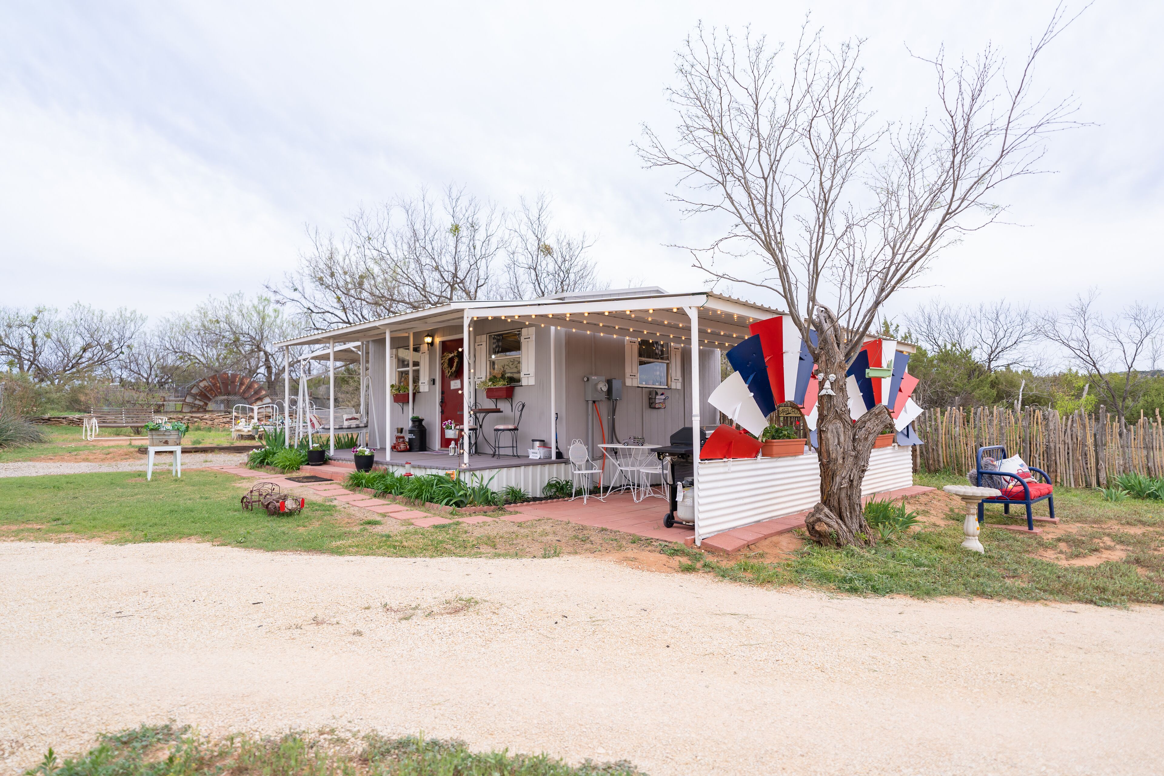 A small, single-story house with a porch, outdoor seating, and a flag display.