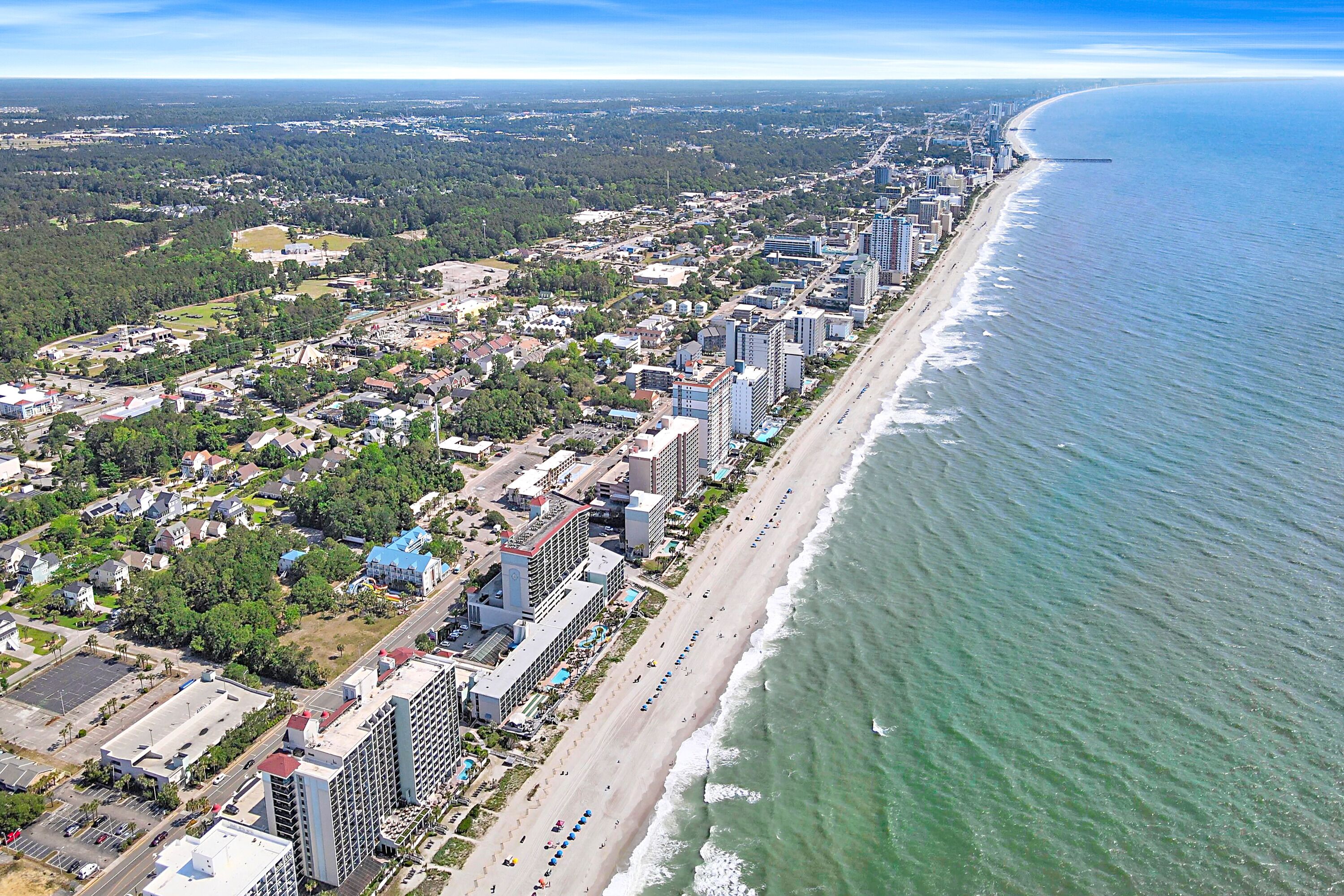An aerial view of a coastal city with a long beachfront, high-rise buildings, and a mix of residential and commercial areas.