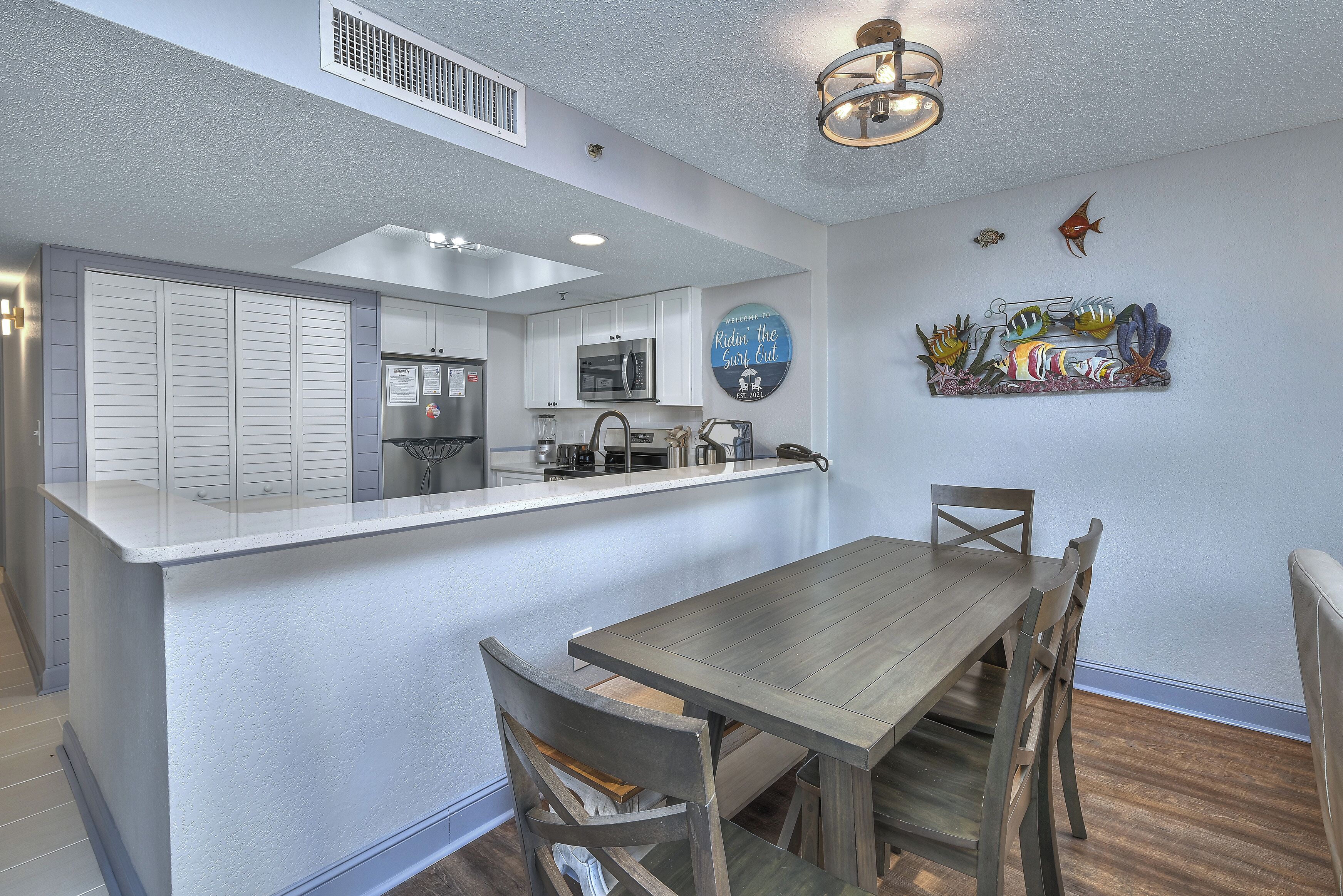 A modern kitchen with white cabinets, a central island, and a dining area with wooden chairs.