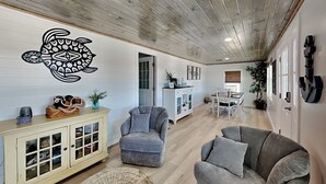 Uma sala de estar espaçosa com teto de madeira, um sofá cinza, uma poltrona cinza, um armário com portas de vidro e um objeto decorativo na parede.