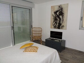 A bedroom with a bed, a chair, a TV, and a painting on the wall.