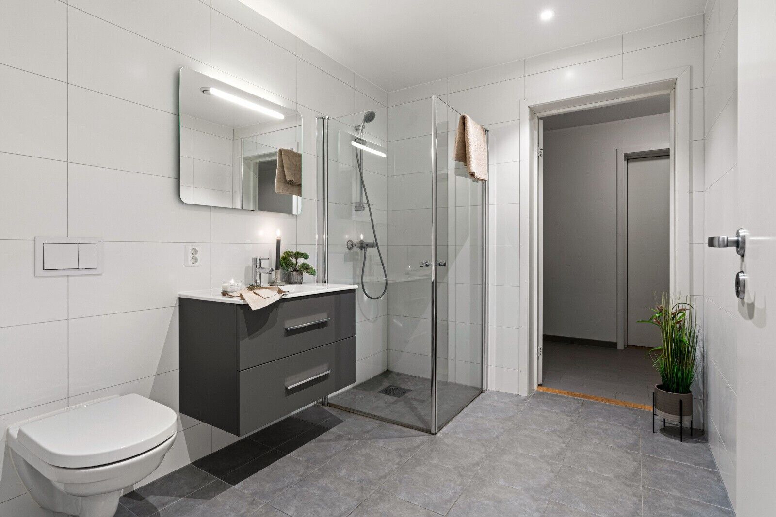 A modern bathroom with a toilet, a dark vanity, a glass shower enclosure, and a potted plant.