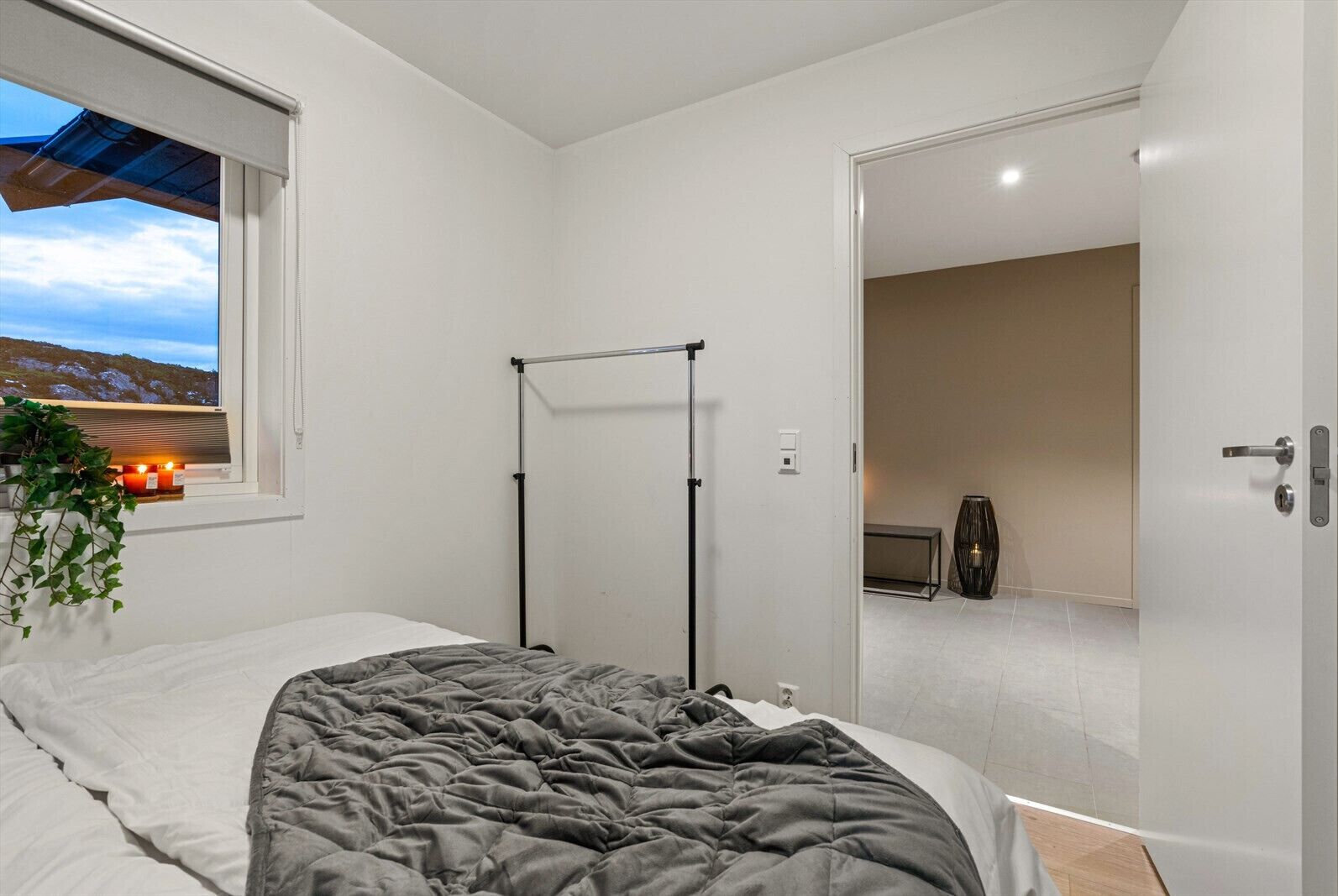 Een slaapkamer met een bed, een raam met uitzicht op een landschap, een radiator en een deur naar een andere kamer.