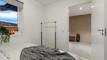 Een slaapkamer met een bed, een raam met uitzicht op een landschap, een radiator en een deur naar een andere kamer.