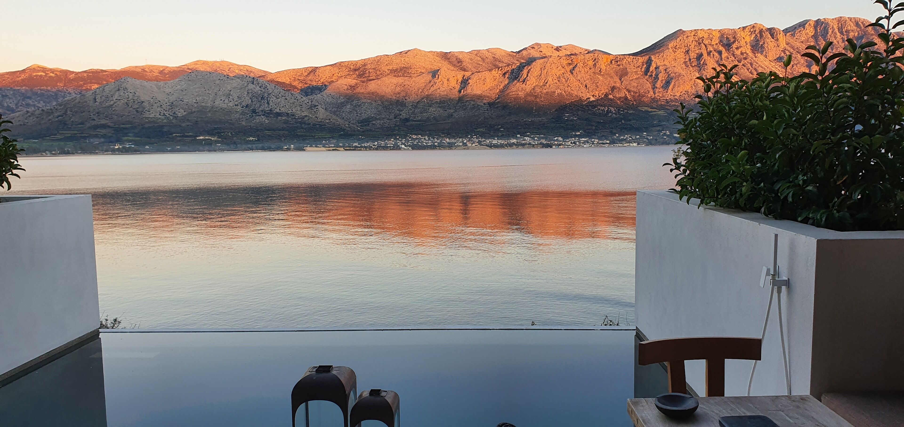 A terrace with a view of a lake and mountains, featuring a table and chairs.