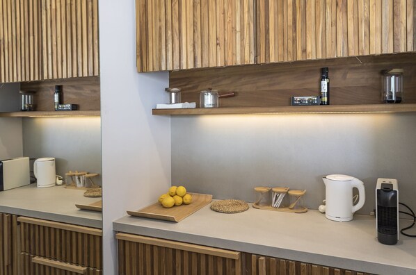 A modern kitchen with wooden cabinetry, a countertop with a cutting board, lemons, a coffee maker, and a kettle.