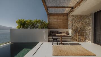A modern outdoor living space with a pool, a seating area with cushions, and a stone wall.