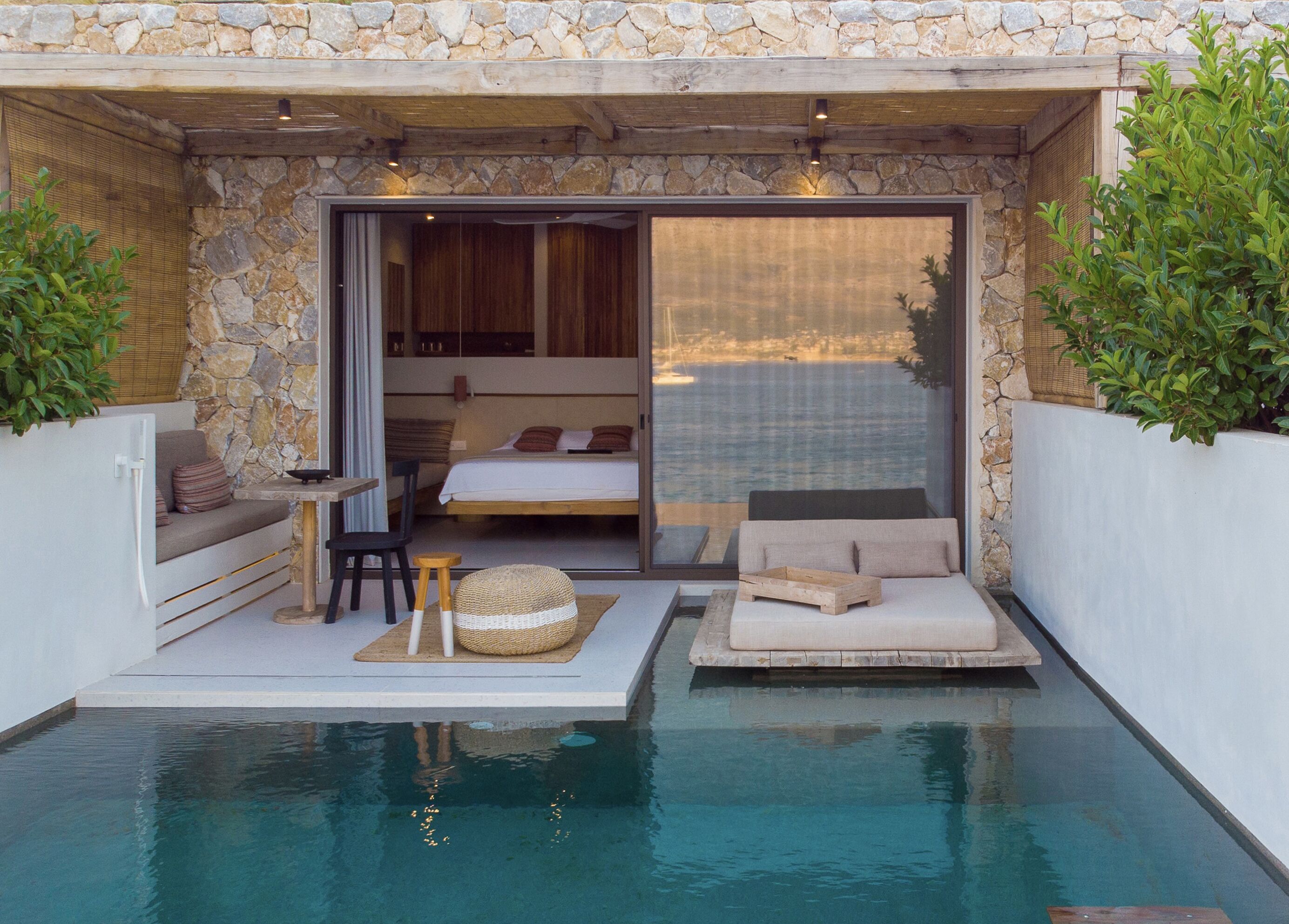 A private pool area with a stone wall, a bed, a seating area, and a view of the sea.