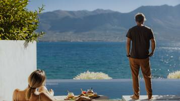 A couple relaxing by a pool with a view of the sea and mountains.