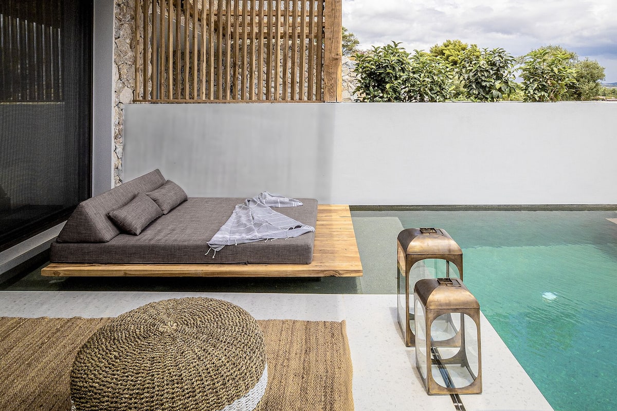 Un área de estar al aire libre con piscina, un banco de madera y un sofá con cojines.