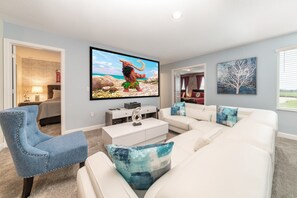 Una sala de estar con un sofá blanco, un sillón azul, un televisor de pantalla plana y una mesa de centro.