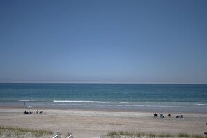 A beach with a clear sky, calm sea, and a few people and beach chairs.