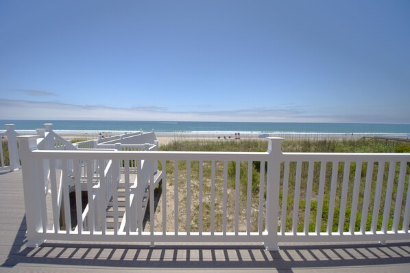 A wooden deck with a white railing overlooking a beach.