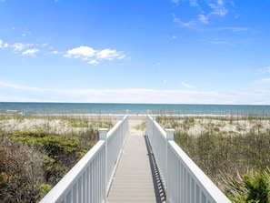 A wooden boardwalk leading to a beach with a clear sky.