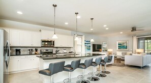 A modern kitchen with white cabinets, a central island with bar stools, and a dining area with a sofa and table.