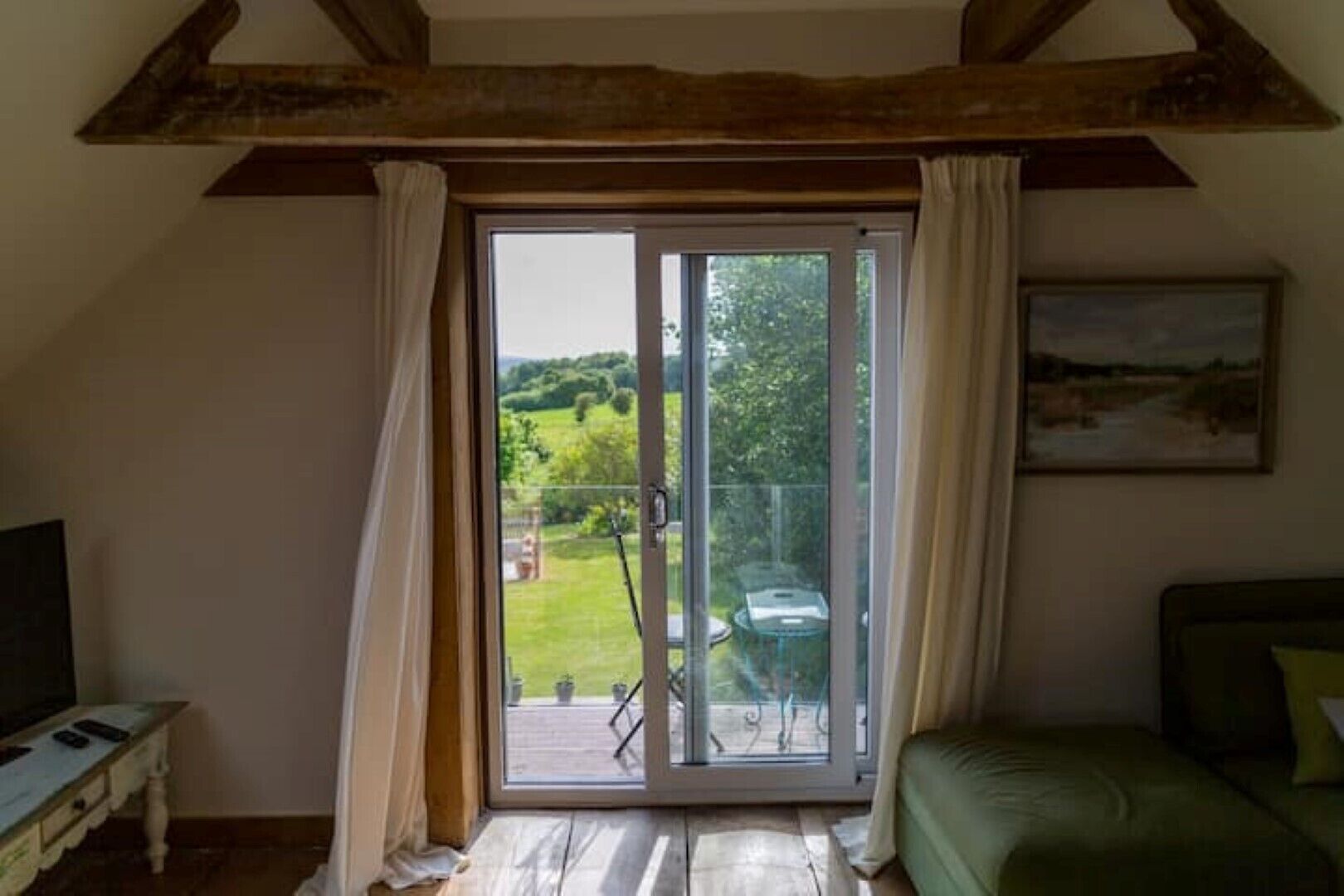 Une pièce dotée d’une grande porte-fenêtre coulissante donnant sur un balcon avec vue sur la verdure. On y trouve un lit recouvert d’une couverture verte, une petite table avec un téléviseur et un tableau accroché au mur.